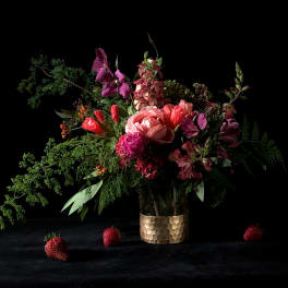 Mixed bouquet in a gold textured vase with strawberries on a dark surface
