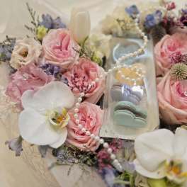 Pink roses and white orchids arranged around a clear box of macarons