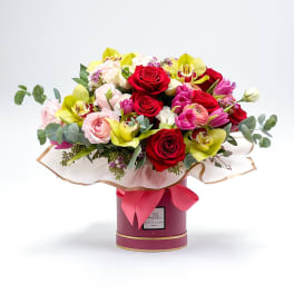 Bouquet of red roses, pink blooms, and yellow orchids in a round box