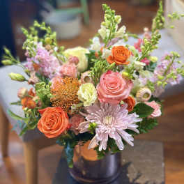 Mixed arrangement of pink and orange roses, mums, and snapdragons in a metallic vase