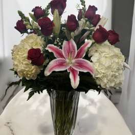 Bouquet of red roses, white hydrangeas, and a pink lily in a clear vase