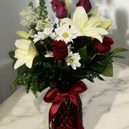 Red roses and white lilies in a red glass vase with a satin bow