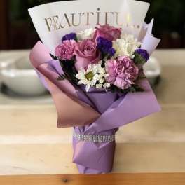 Pink and purple bouquet with roses, carnations, and daisies in decorative wrap