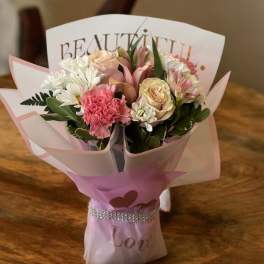 Pink and white bouquet wrapped in decorative paper with a ribbon