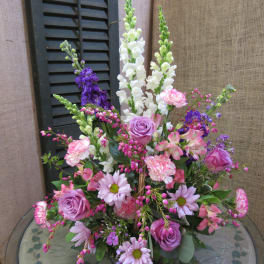 Mixed pink and purple floral arrangement with tall white spikes in a glass vase