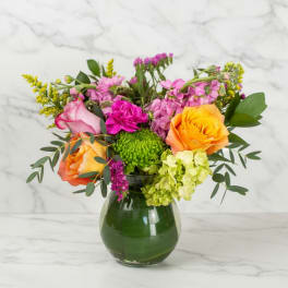 Mixed arrangement of orange roses and bright pink blooms in a round glass vase
