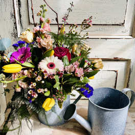 Mixed bouquet in a metal watering can with pink, yellow, white, and purple flowers