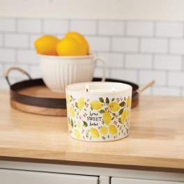 Lemon-patterned candle on a wooden counter with a bowl of lemons behind it
