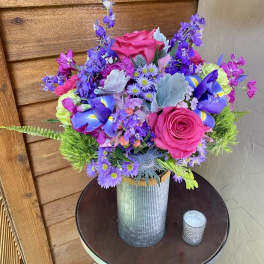 Bright mixed bouquet in a ribbed metal vase with pink roses and purple flowers