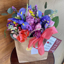 Colorful bouquet in a brown paper bag with a pink ribbon