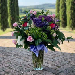 Bouquet of pink and purple flowers in a clear glass vase with a lavender ribbon