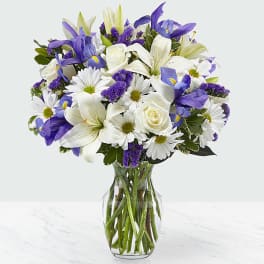Bouquet of white lilies, roses, and purple flowers in a glass vase