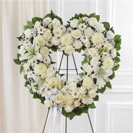 Heart-shaped white floral wreath on a stand with a ribbon bow