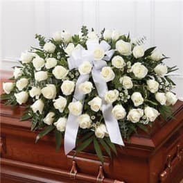 White rose casket spray with a white ribbon on a wooden casket