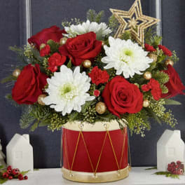 Red roses and white daisies arranged in a red drum vase with gold accents