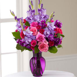 Pink and purple flower arrangement in a purple glass vase