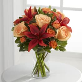 Bouquet of peach roses and red lilies in a clear glass vase