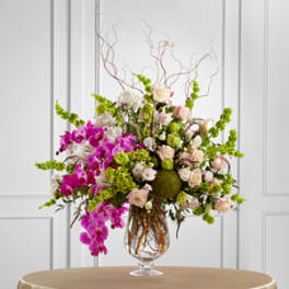 Tall floral arrangement with pink orchids and pale roses in a glass vase
