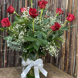 Red roses in a glass vase with baby's breath and a white ribbon