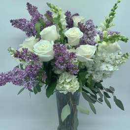 White roses and purple lilacs arranged in a clear glass vase