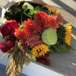 Bouquet of orange dahlias, red peonies, and yellow sunflowers with a lotus pod
