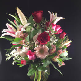 Mixed bouquet of red roses, lilies, and pink daisies in a glass vase