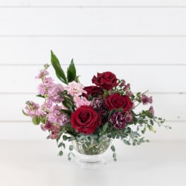 Red and pink roses in a clear glass vase with mixed greenery
