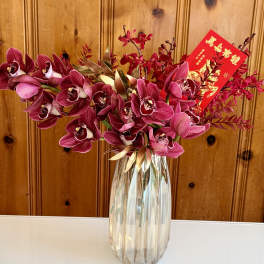Pink orchids arranged in a clear glass vase with a red envelope card