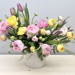Pastel arrangement of pink, yellow and lavender blooms with tulips in a white ceramic vase