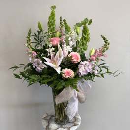 Pink lilies and roses in a glass vase with green spikes