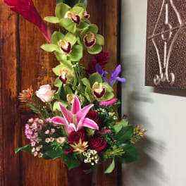 Tall mixed bouquet with orchids, lilies, and roses in a dark vase