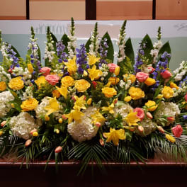 Large stage arrangement of yellow lilies, roses, white hydrangea, and blue delphinium.