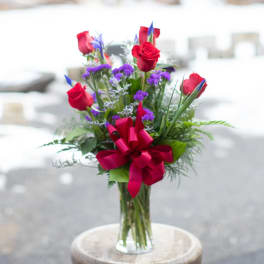 Bouquet of red roses and purple flowers in a clear glass vase
