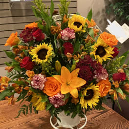 Mixed bouquet in a white container with sunflowers, roses, and lilies
