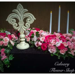 Pink rose arrangements with a decorative fleur-de-lis and tall candles
