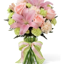 Pink lilies and roses in a glass vase with a striped ribbon
