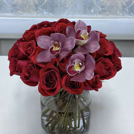 Red roses and pink orchids arranged in a clear glass vase