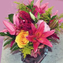 Bright pink lilies and a yellow rose arranged in a clear glass cube vase.