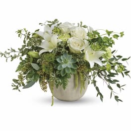 White lilies and roses in a round ceramic vase with trailing greenery
