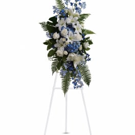 Standing floral spray with white lilies, blue flowers, and ferns on an easel