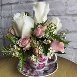 White and pink roses arranged in a floral teacup with saucer