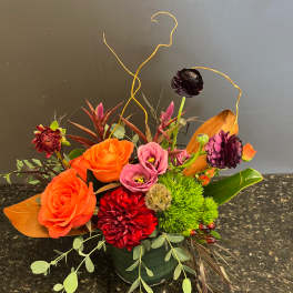 Mixed floral arrangement with orange roses, pink blooms, and red flowers in a green vase