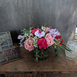 Pink and lavender flower arrangement in a glass vase on a wooden table