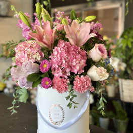 Pink lilies, hydrangeas, roses, and carnations arranged in a round white hatbox.