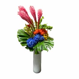 Tropical bouquet with pink plumes, blue hydrangeas, and orange roses in a tall vase