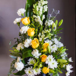 Tall floral arrangement with yellow roses, white blooms, and a black vase