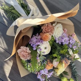 Wrapped bouquet of pastel roses, carnations, and purple blooms