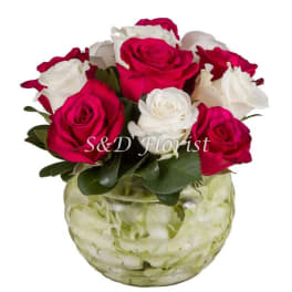 Pink and white roses in a glass vase filled with pale petals