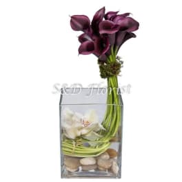 Purple and white calla lilies in a clear square vase with stones