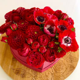 Red floral arrangement in a pink heart-shaped box